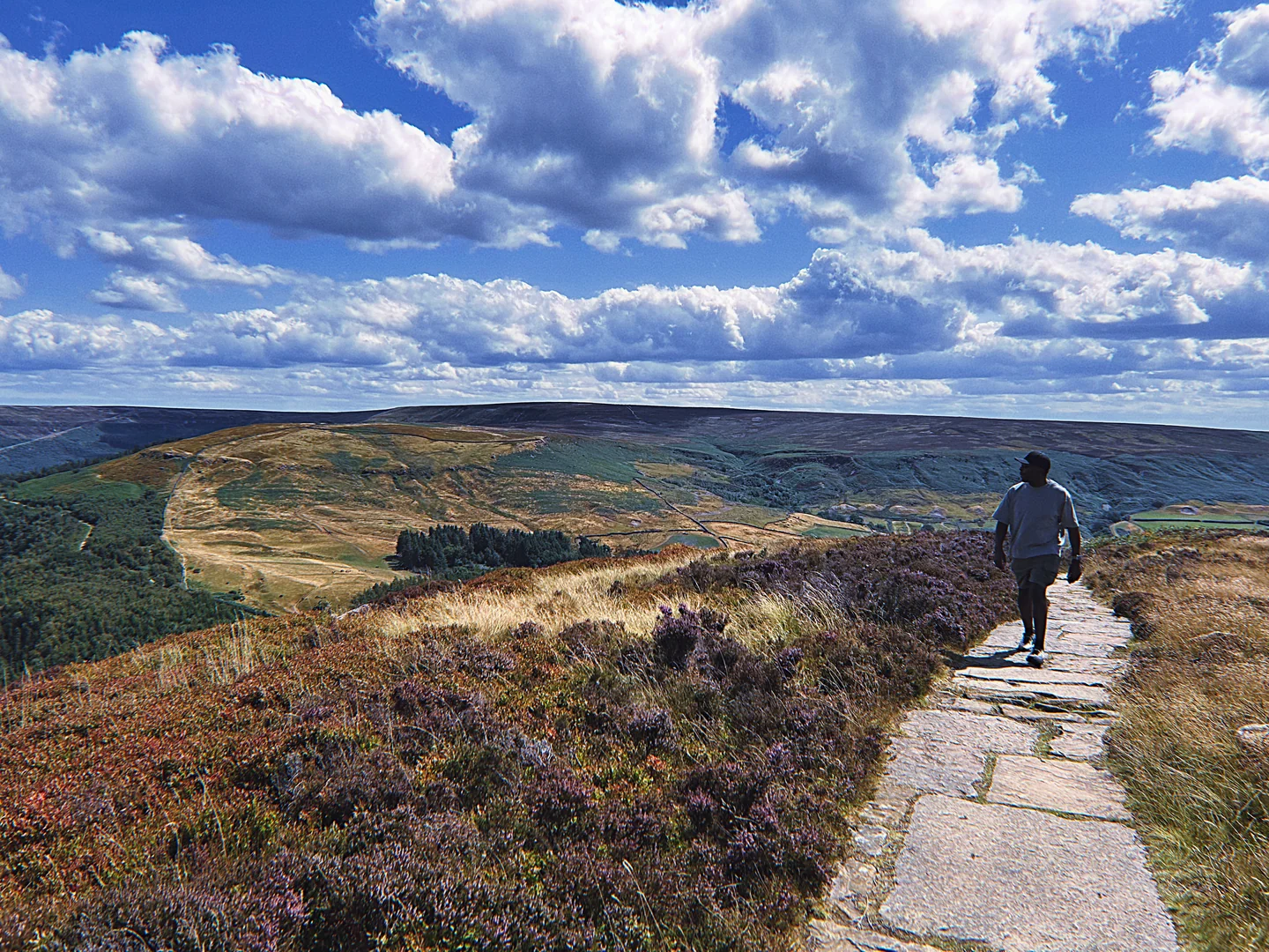 A walker on an open hillside trail beneath a wide blue sky